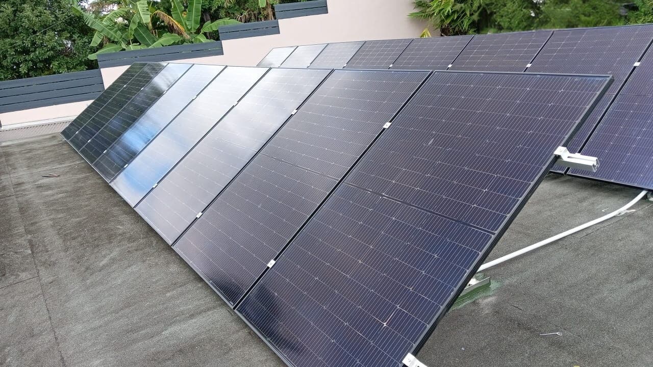 Rangées de panneaux noirs inclinés sur châssis, posées sur un toit plat, La Réunion